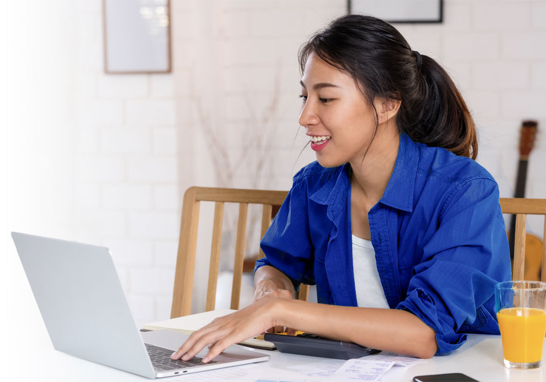 woman wearing a blue shirt working on a laptop and smiling