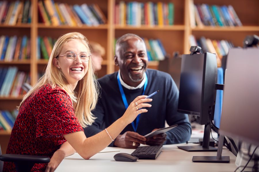 Woman and man sitting by a computer talking in a library