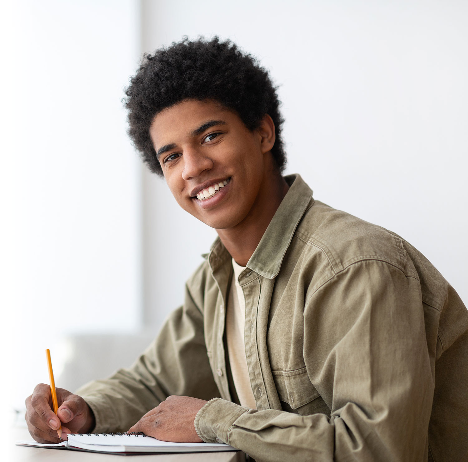 African American UK Student holding a pencil and writing while looking at the viewer.